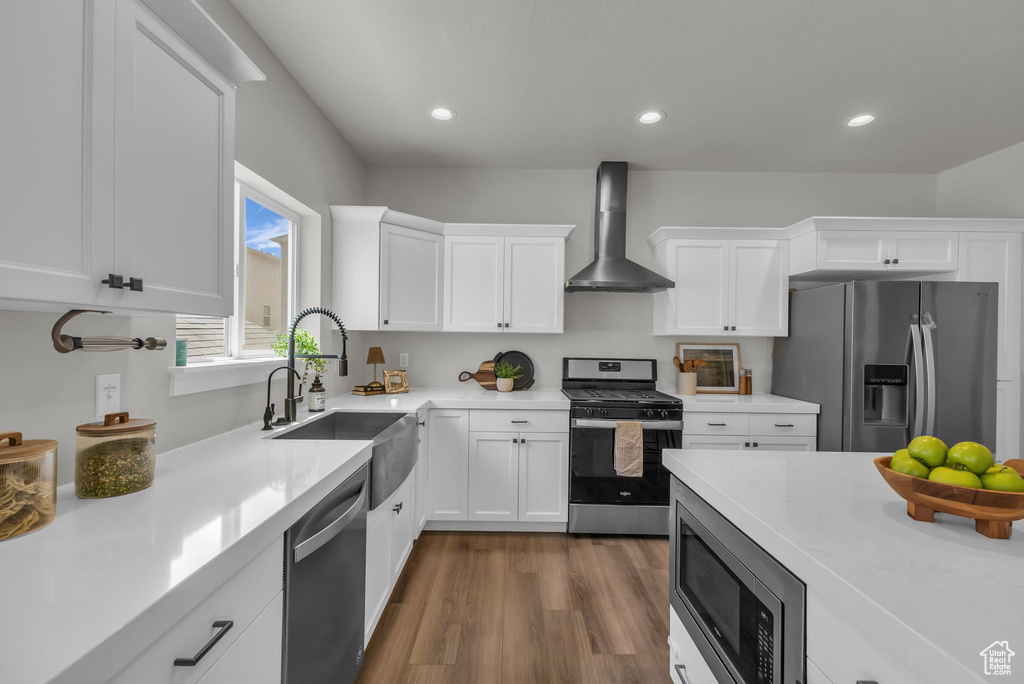 Kitchen featuring appliances with stainless steel finishes, wall chimney range hood, a sink, white cabinetry, and recessed lighting