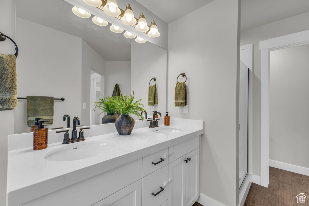 Bathroom with wood finished floors, double vanity, baseboards, and a stall shower