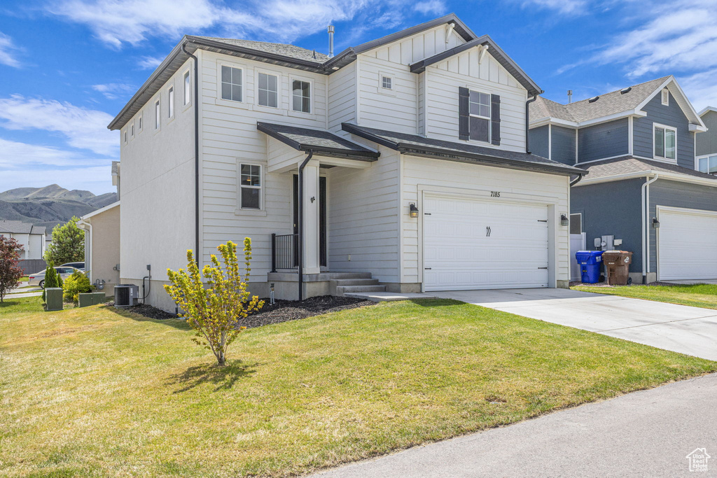 View of front facade with board and batten siding, driveway, an attached garage, central air condition unit, and a front yard