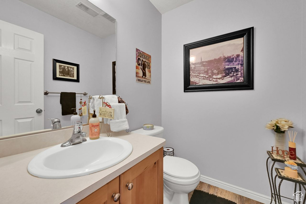 Half bath with wood finished floors, vanity, toilet, and baseboards