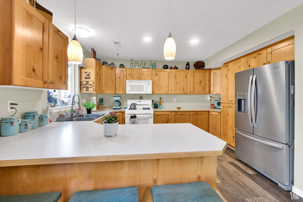 Kitchen featuring white appliances, a sink, a peninsula, light countertops, and hanging light fixtures