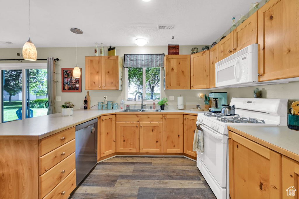 Kitchen featuring white appliances, a sink, a peninsula, dark wood-style floors, and healthy amount of natural light
