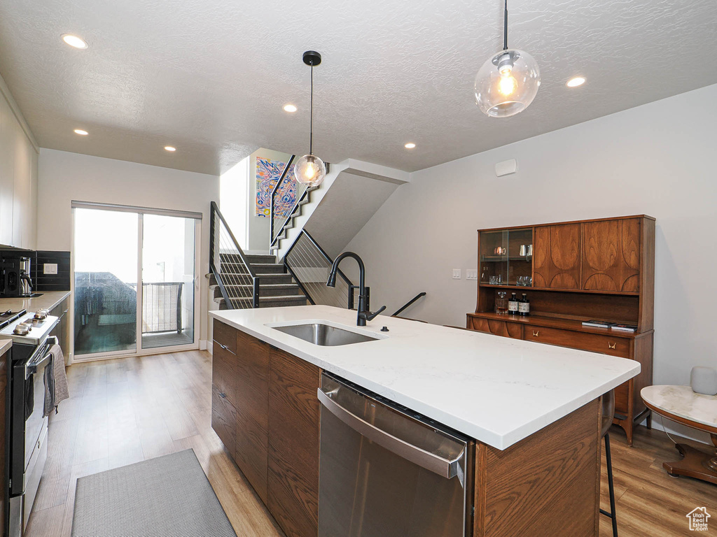 Kitchen with a sink, dishwasher, gas range oven, light wood-type flooring, and a textured ceiling