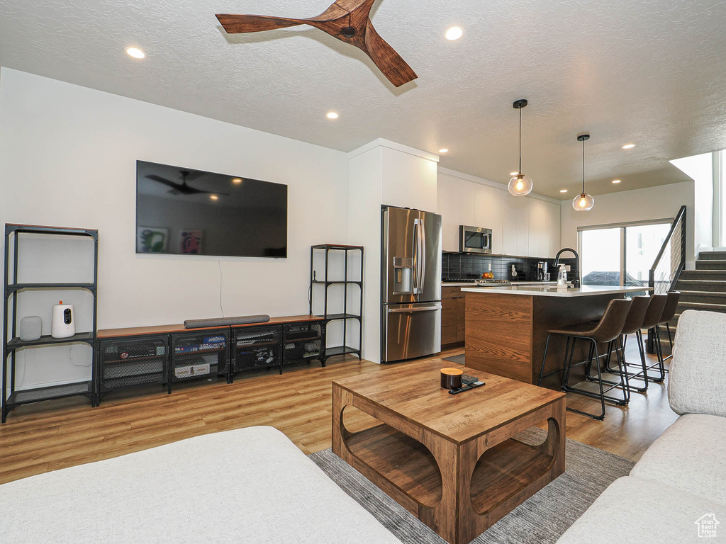 Living room featuring ceiling fan, light wood-style flooring, recessed lighting, and a textured ceiling