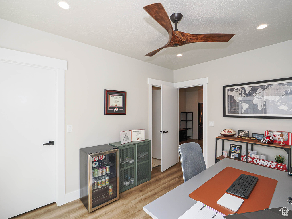 Office area featuring light wood-style floors, recessed lighting, ceiling fan, and beverage cooler