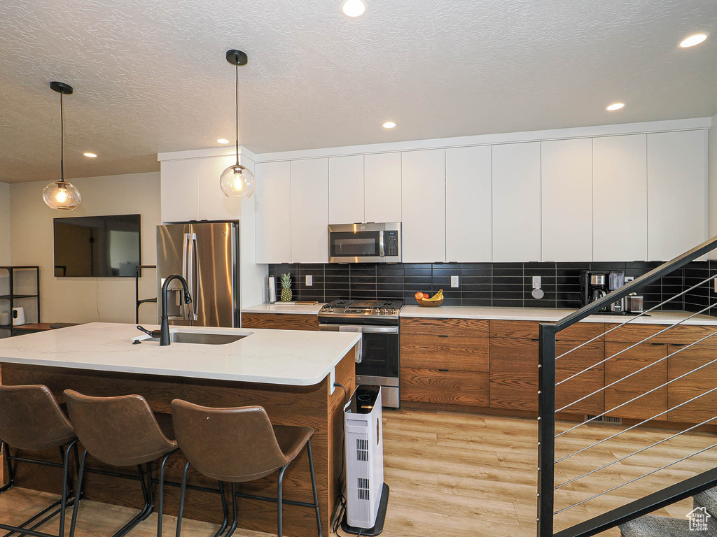 Kitchen featuring appliances with stainless steel finishes, light wood-style floors, white cabinets, recessed lighting, and backsplash