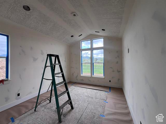 Unfurnished bedroom featuring a textured ceiling, lofted ceiling, and baseboards