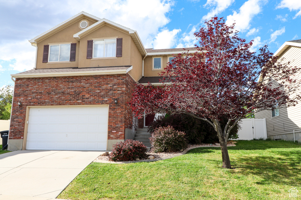 View of front of home with an attached garage, driveway, stucco siding, and brick siding