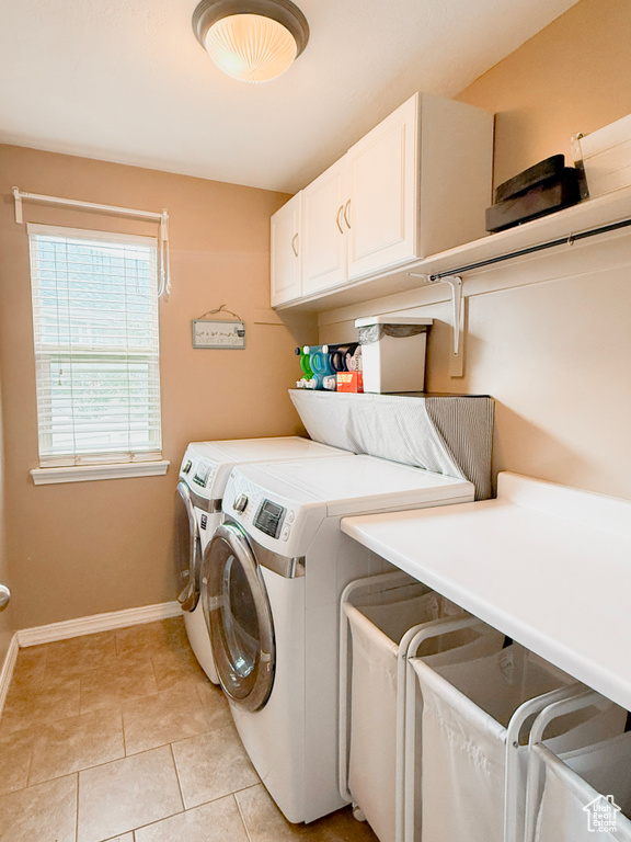 Washroom with cabinet space, washer and clothes dryer, baseboards, and light tile patterned flooring