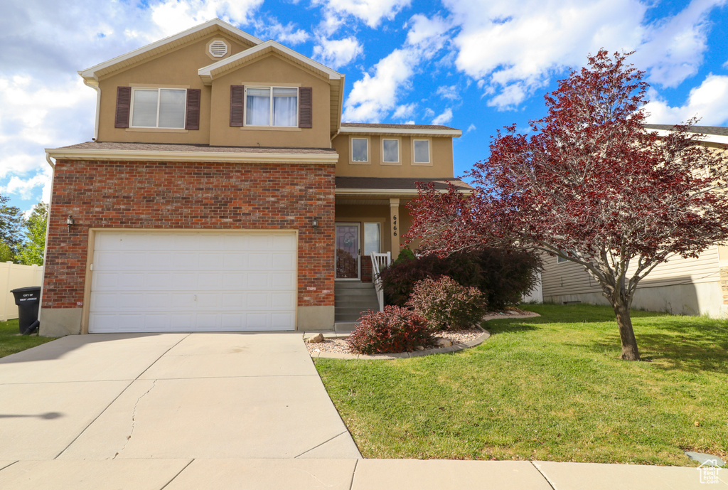 Traditional-style house with a garage, a front yard, driveway, and brick siding