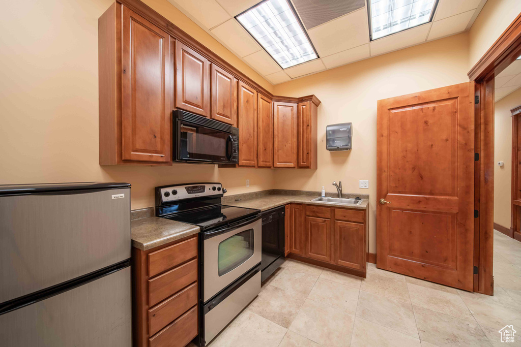 Kitchen with black appliances, a sink, brown cabinetry, a drop ceiling, and light tile patterned floors