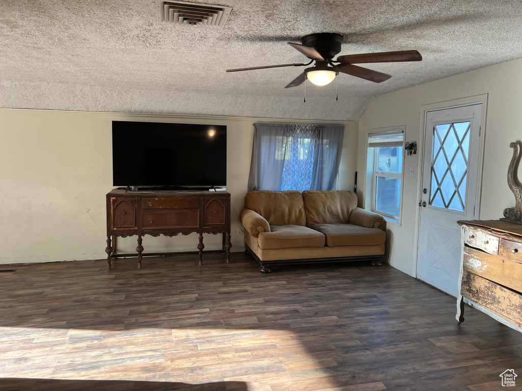 Living area with ceiling fan, a textured ceiling, wood finished floors, and vaulted ceiling