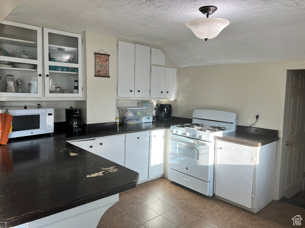 Kitchen featuring white appliances, dark countertops, white cabinetry, a textured ceiling, and glass insert cabinets