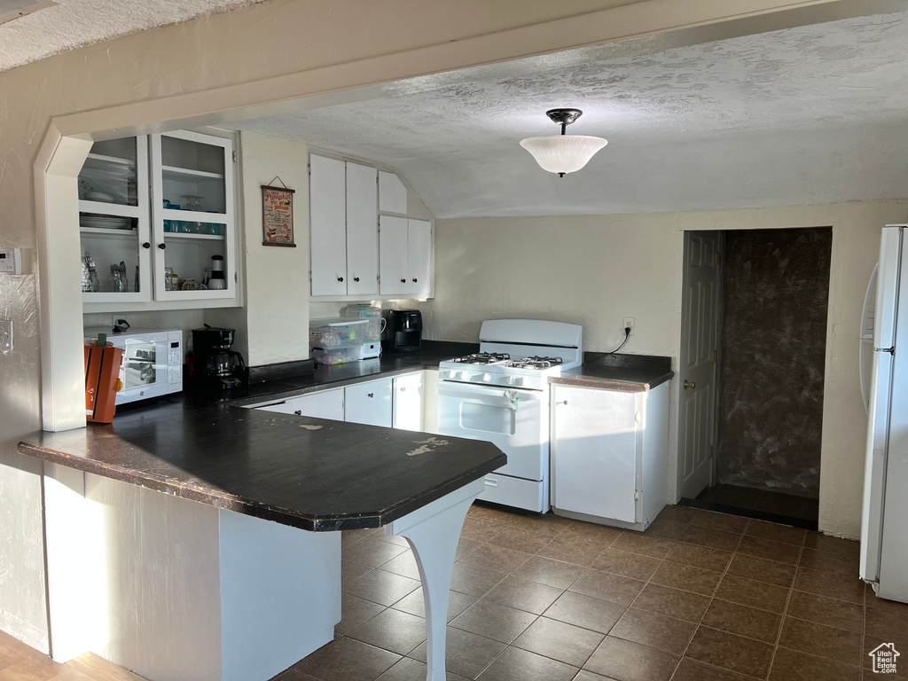 Kitchen with white appliances, dark countertops, a peninsula, white cabinets, and dark tile patterned flooring