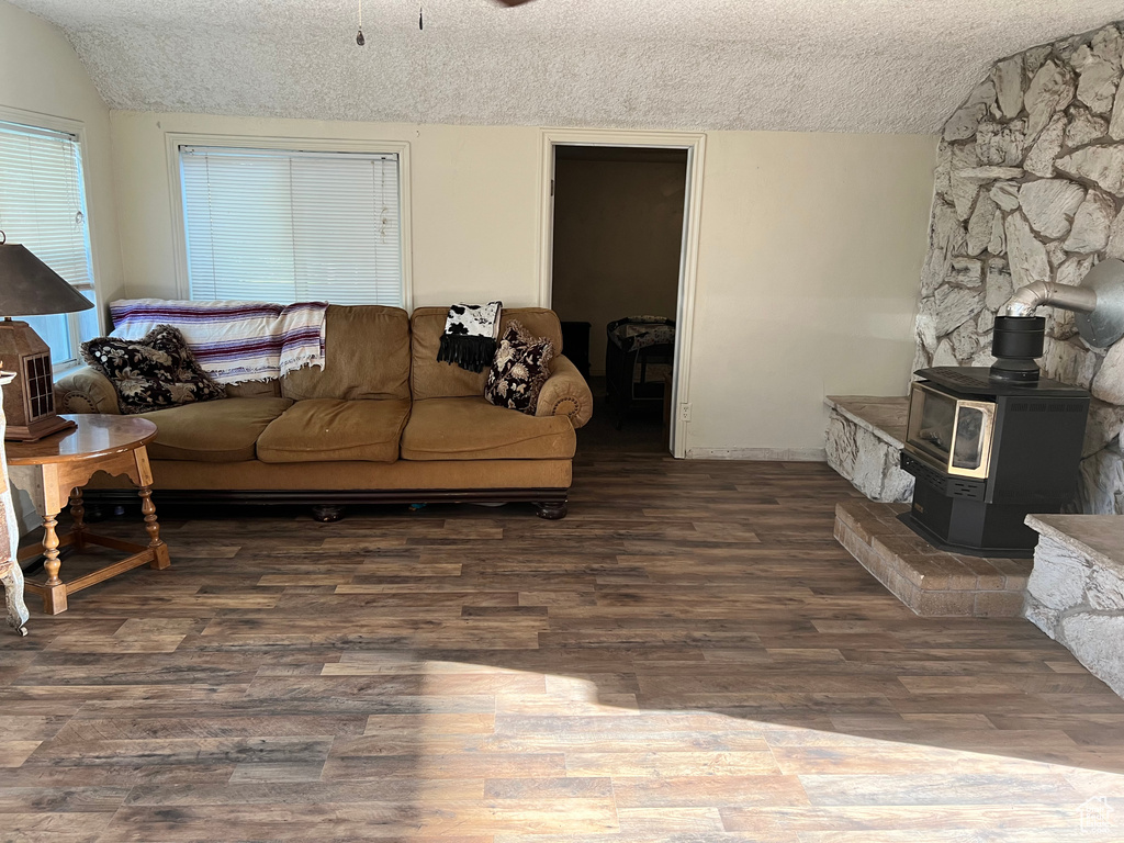 Living area with a textured ceiling, wood finished floors, a wood stove, vaulted ceiling, and baseboards