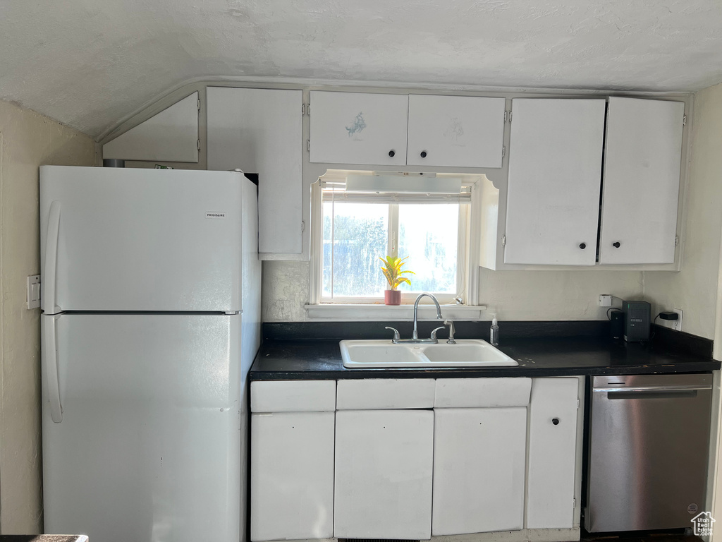 Kitchen with freestanding refrigerator, a sink, dishwasher, dark countertops, and white cabinets