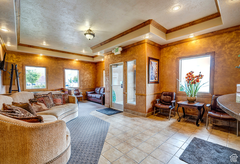 Living room featuring a textured ceiling, crown molding, light tile patterned floors, and a tray ceiling