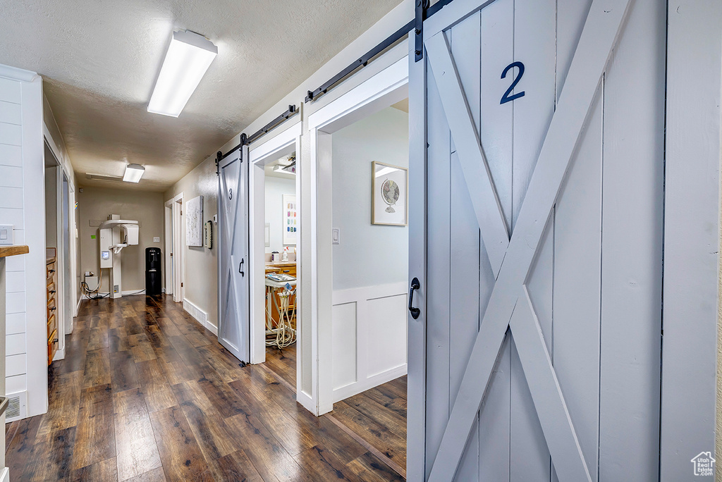 Hall featuring a barn door, dark wood-type flooring, and a textured ceiling