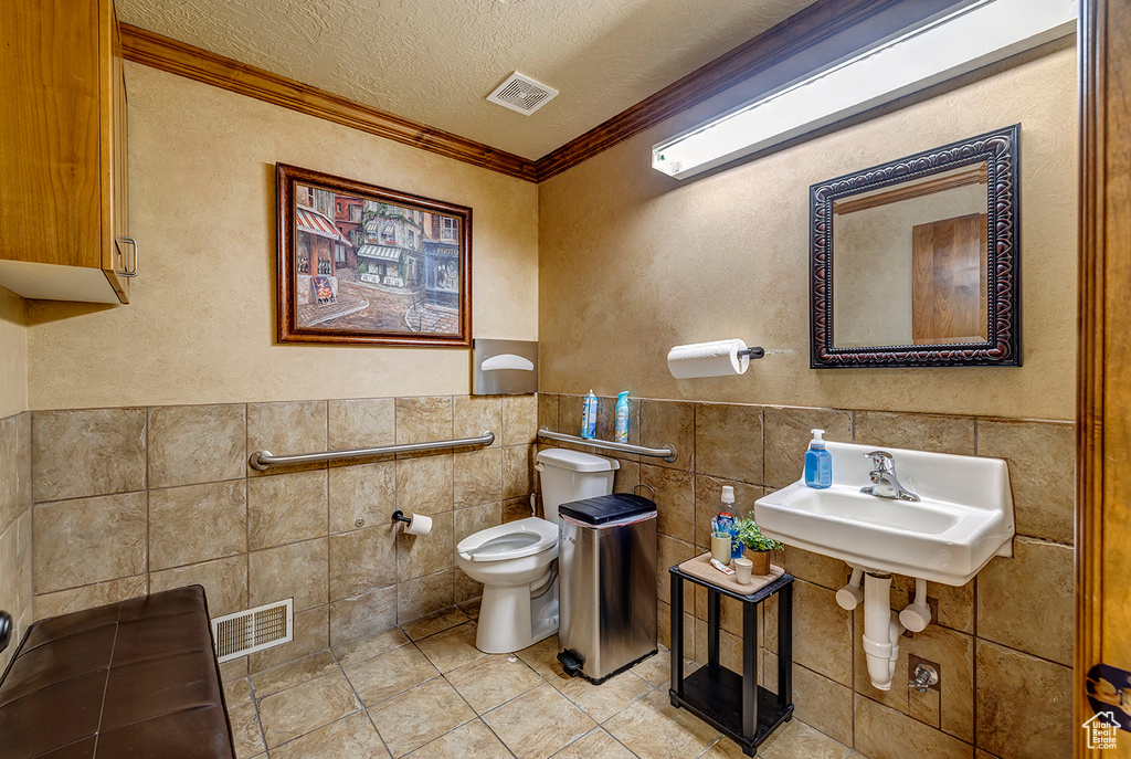 Bathroom with tile walls, ornamental molding, toilet, a textured ceiling, and tile patterned flooring