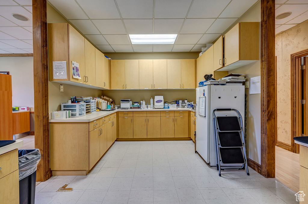 Kitchen featuring a drop ceiling, freestanding refrigerator, light countertops, light brown cabinets, and light floors
