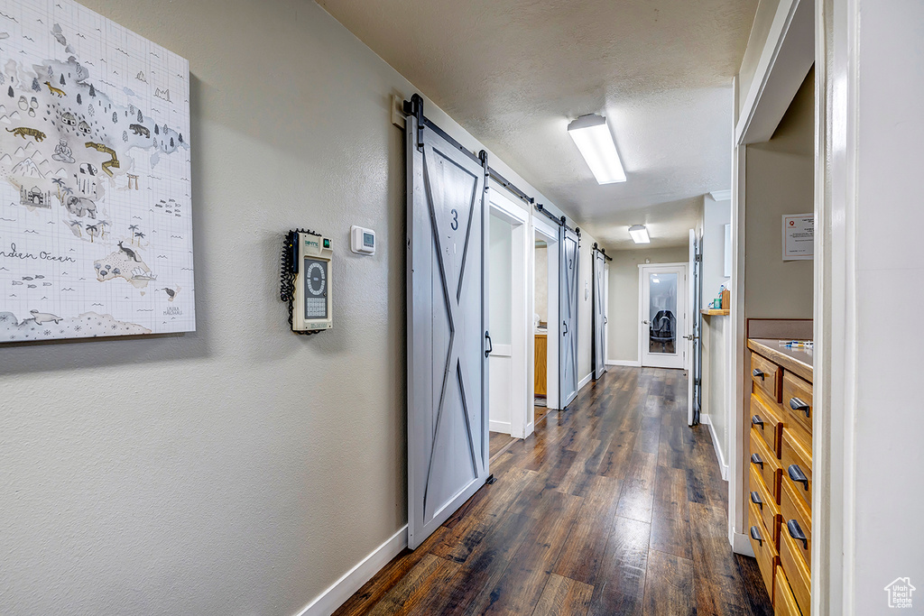 Hall with a barn door, dark wood-type flooring, and baseboards