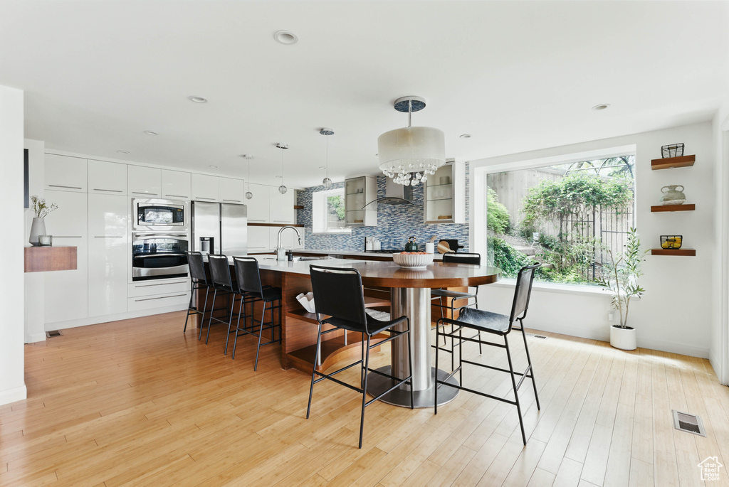 Kitchen featuring appliances with stainless steel finishes, a breakfast bar, backsplash, light wood-type flooring, and decorative light fixtures