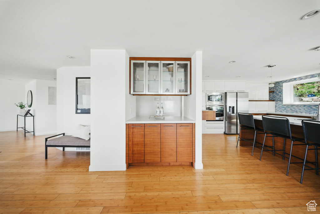 Bar area featuring stainless steel appliances, tasteful backsplash, light wood finished floors, and pendant lighting