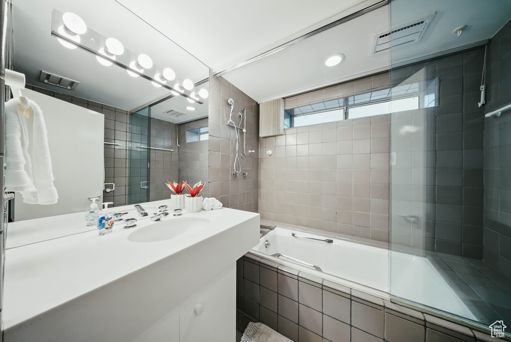 Full bath with tiled shower / bath combo, vanity, and tile walls
