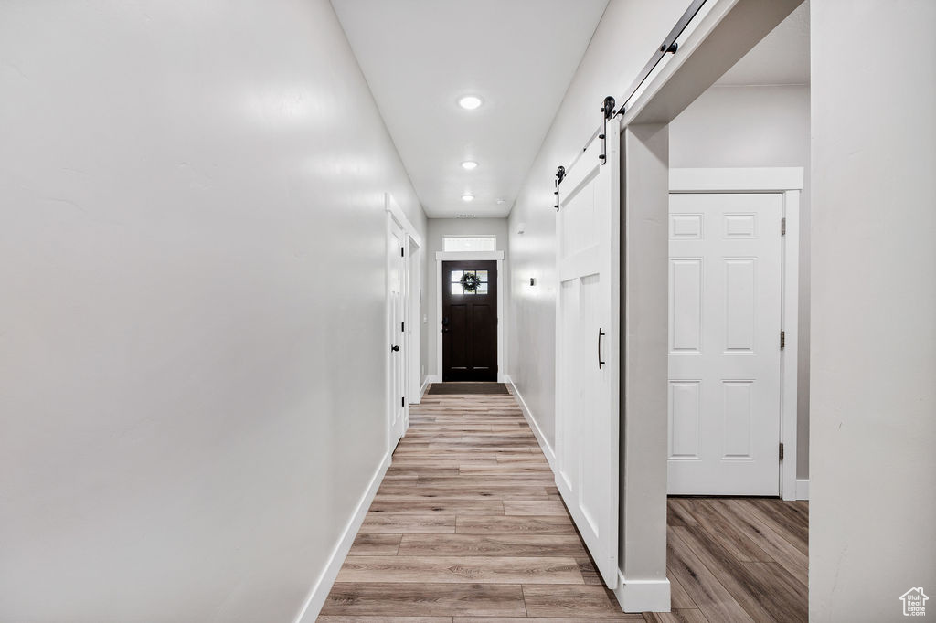 Corridor with light wood-style flooring, a barn door, recessed lighting, and baseboards