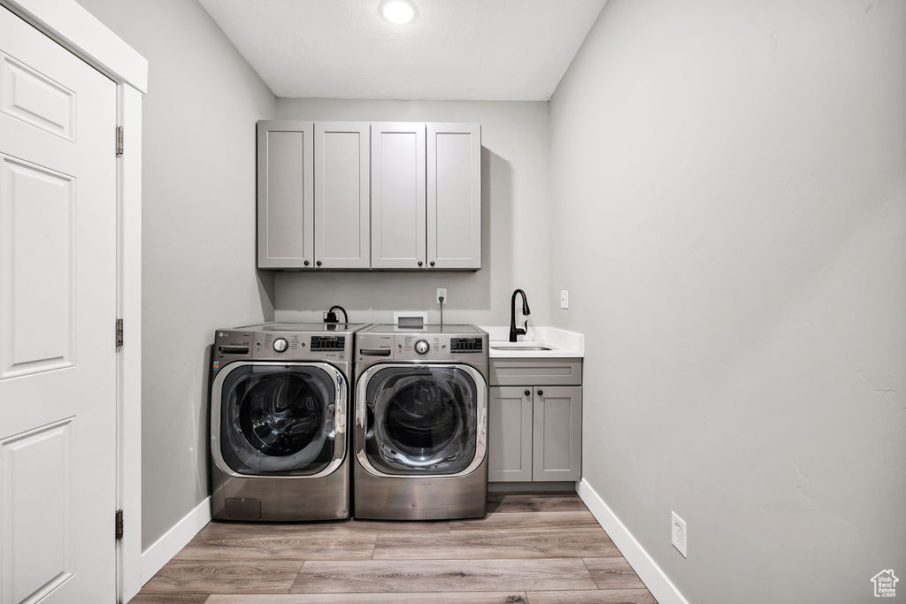 Washroom featuring cabinet space, washing machine and dryer, baseboards, and light wood-type flooring