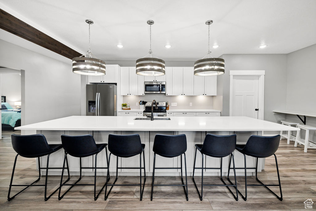 Kitchen with stainless steel appliances, a large island, recessed lighting, light wood finished floors, and white cabinetry