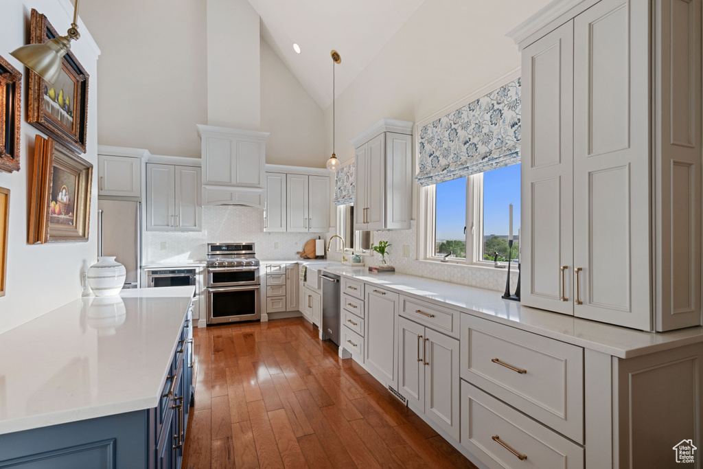 Kitchen with appliances with stainless steel finishes, backsplash, light countertops, high vaulted ceiling, and hardwood / wood-style floors