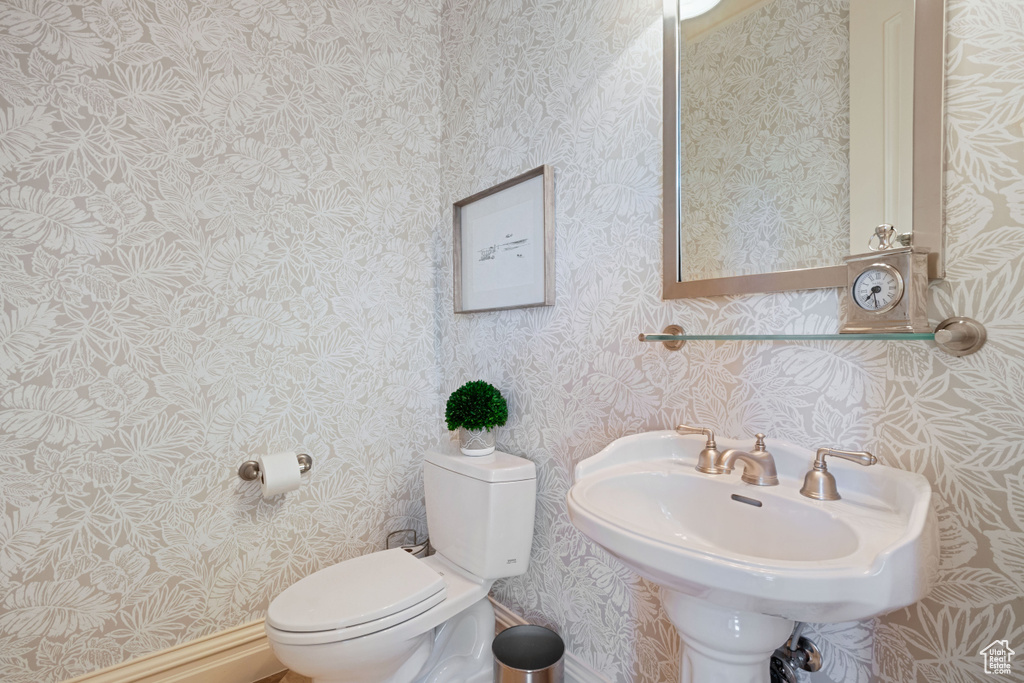 Half bathroom with toilet, wallpapered walls, and a sink