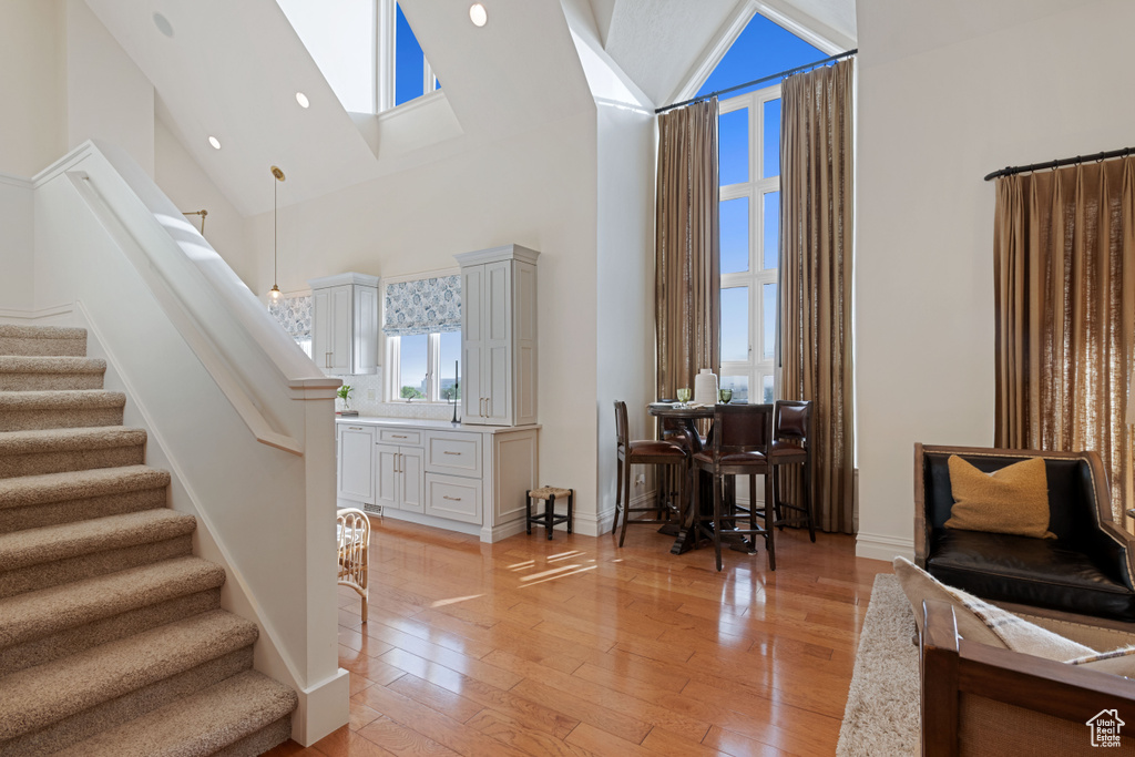 Living room featuring high vaulted ceiling, stairway, light wood-style floors, a skylight, and baseboards