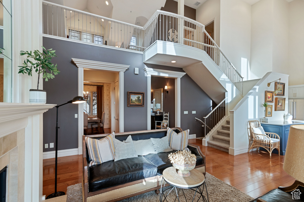 Living room with wood-type flooring, stairs, a towering ceiling, baseboards, and a tiled fireplace