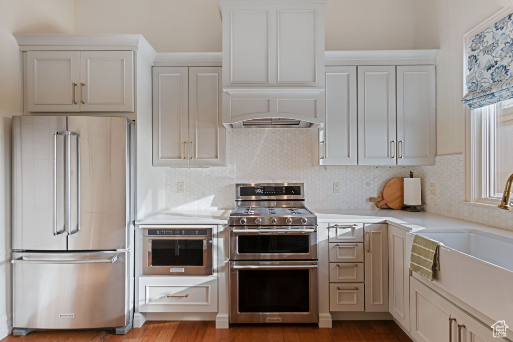 Kitchen featuring appliances with stainless steel finishes, light countertops, a sink, backsplash, and wood finished floors