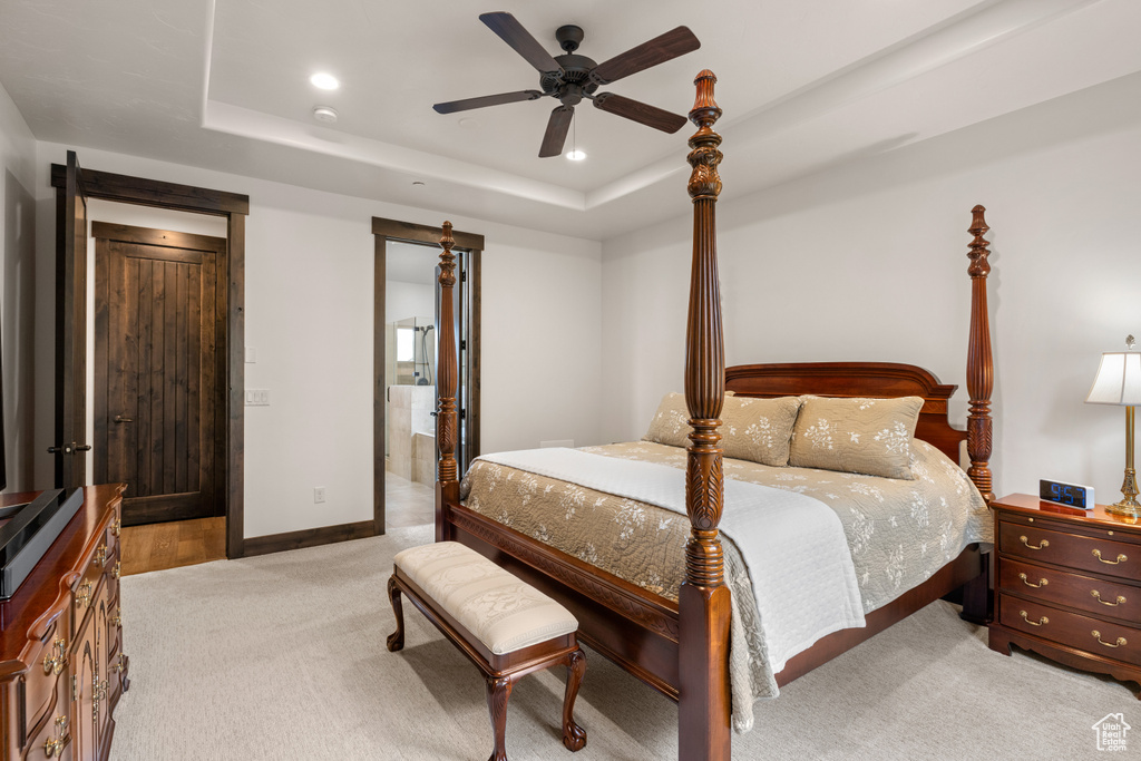 Bedroom featuring light colored carpet, a raised ceiling, recessed lighting, ensuite bathroom, and baseboards