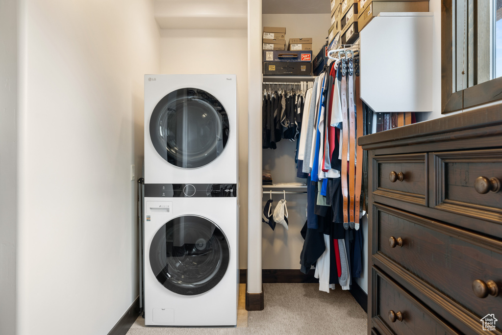 Laundry area featuring stacked washer and clothes dryer, light colored carpet, and baseboards