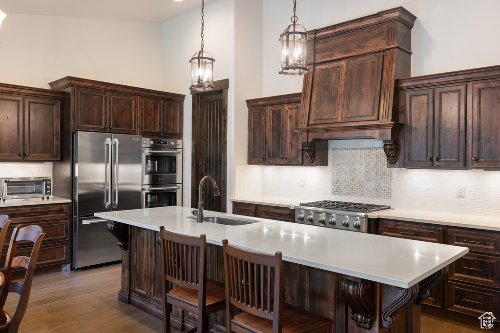 Kitchen with appliances with stainless steel finishes, a sink, tasteful backsplash, light countertops, and a kitchen breakfast bar