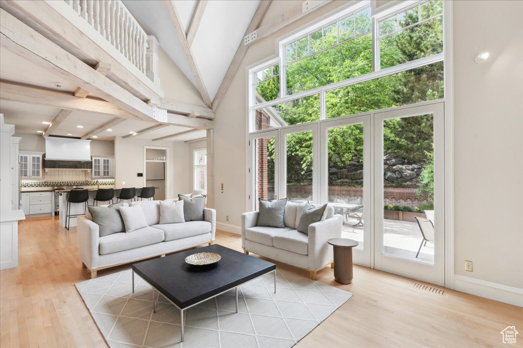 Living area featuring light wood-style flooring, beam ceiling, baseboards, and high vaulted ceiling