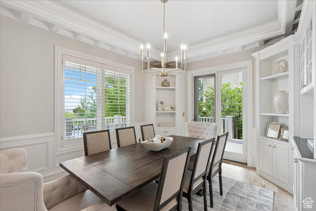 Dining area with healthy amount of natural light, a chandelier, light wood-type flooring, built in shelves, and wainscoting