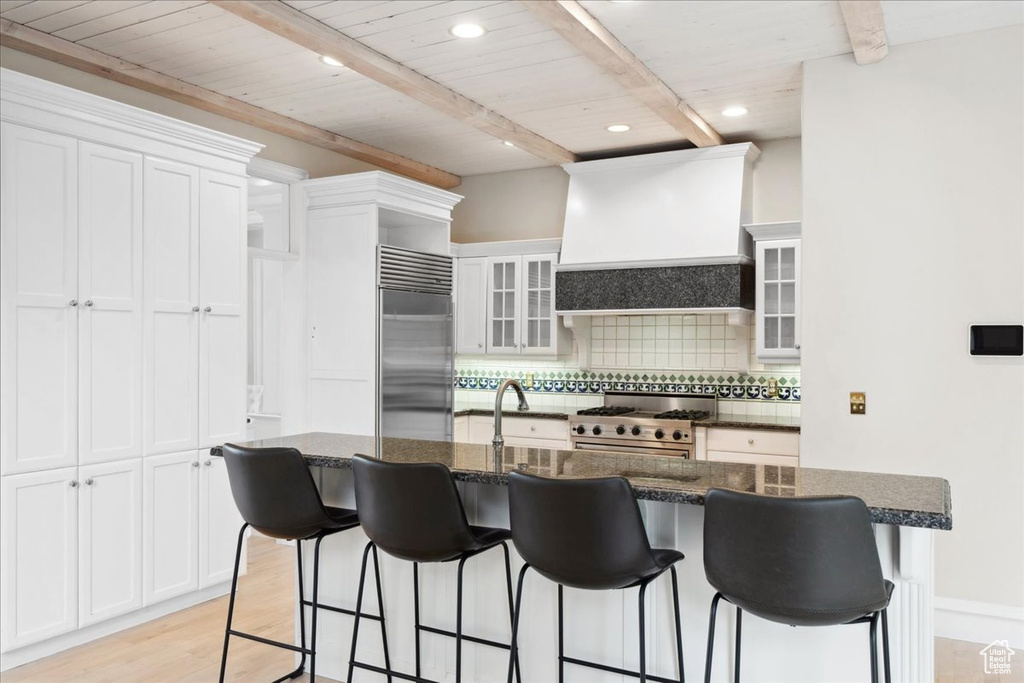 Kitchen with high quality appliances, custom range hood, backsplash, a breakfast bar, and recessed lighting