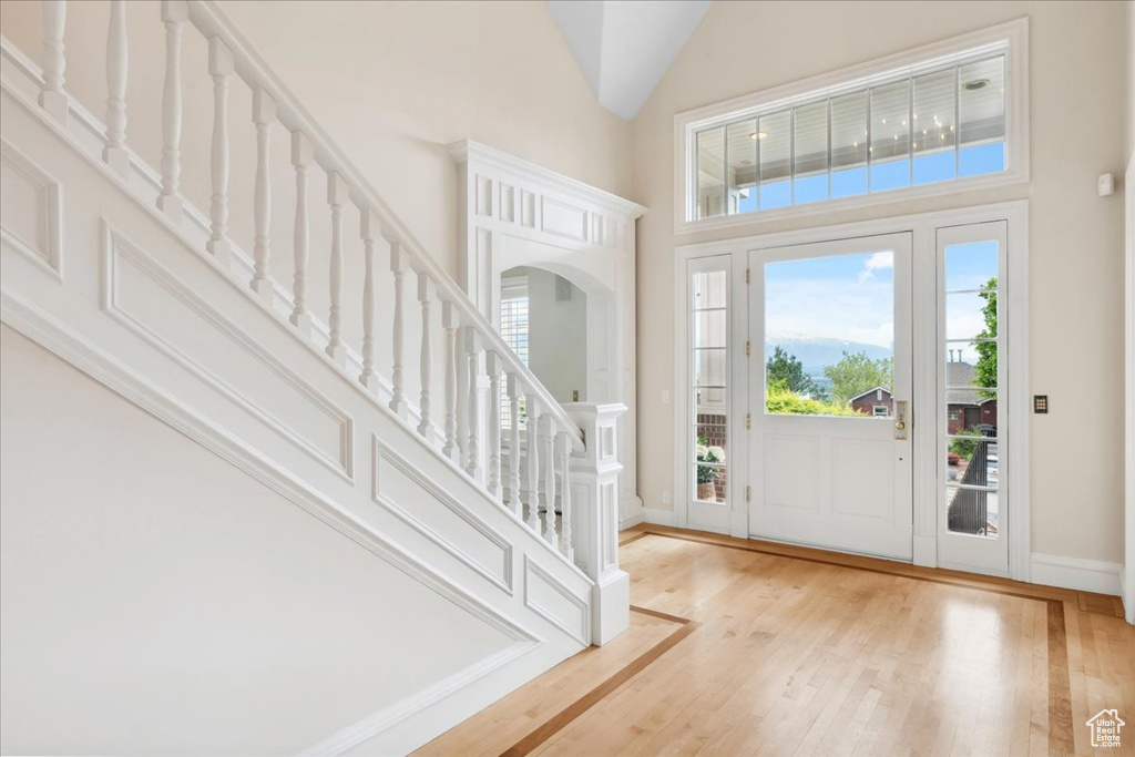 Entrance foyer featuring high vaulted ceiling, healthy amount of natural light, wood finished floors, stairway, and baseboards