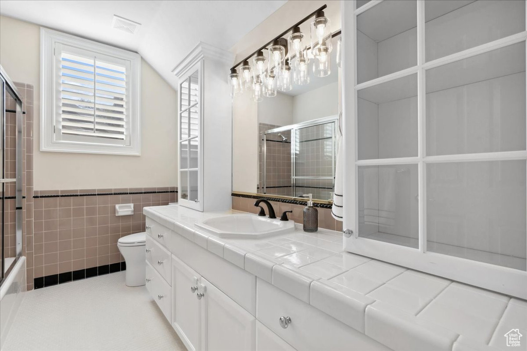 Full bath with toilet, vanity, tile walls, a wainscoted wall, and lofted ceiling