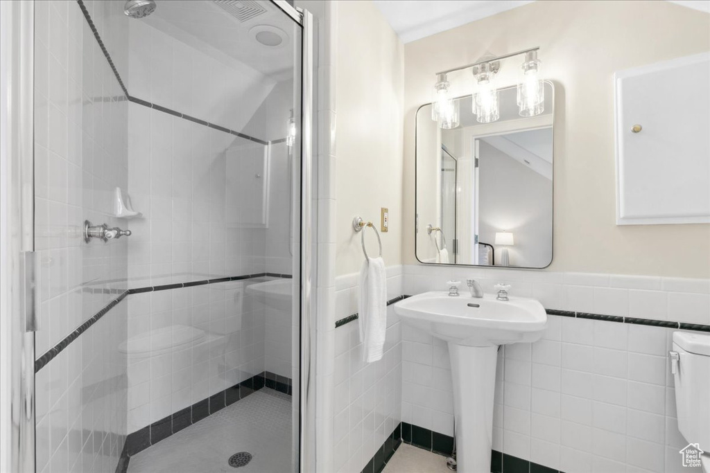 Bathroom featuring tile walls, a shower stall, a wainscoted wall, toilet, and a sink