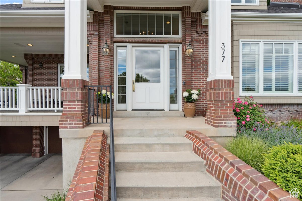 View of exterior entry featuring covered porch, brick siding, and roof with shingles