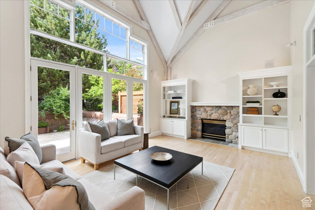 Living room with high vaulted ceiling, light wood-style flooring, beamed ceiling, a fireplace, and baseboards