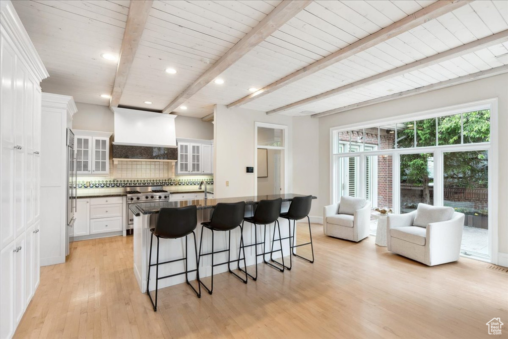Kitchen with high quality appliances, a breakfast bar area, backsplash, white cabinets, and light wood finished floors