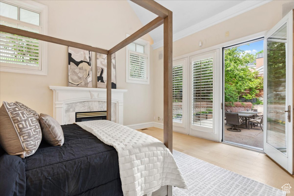 Bedroom featuring access to outside, light wood-type flooring, a fireplace, and crown molding
