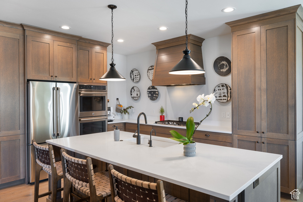 Kitchen with stainless steel appliances, a sink, a breakfast bar, pendant lighting, and light countertops